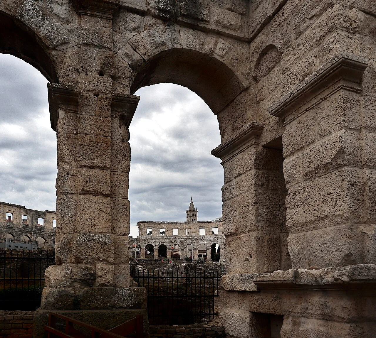 Stone arches of Pula Arena framing a view of the amphitheatre's outer wall