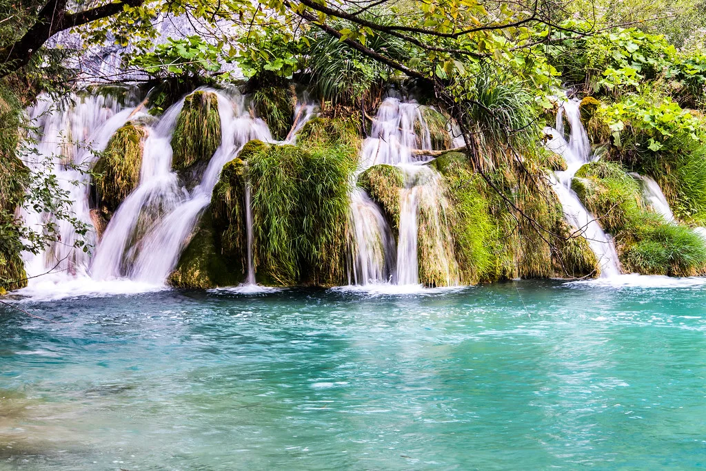 Waterfalls pouring into a turquoise pool in Plitvice Lakes National Park.