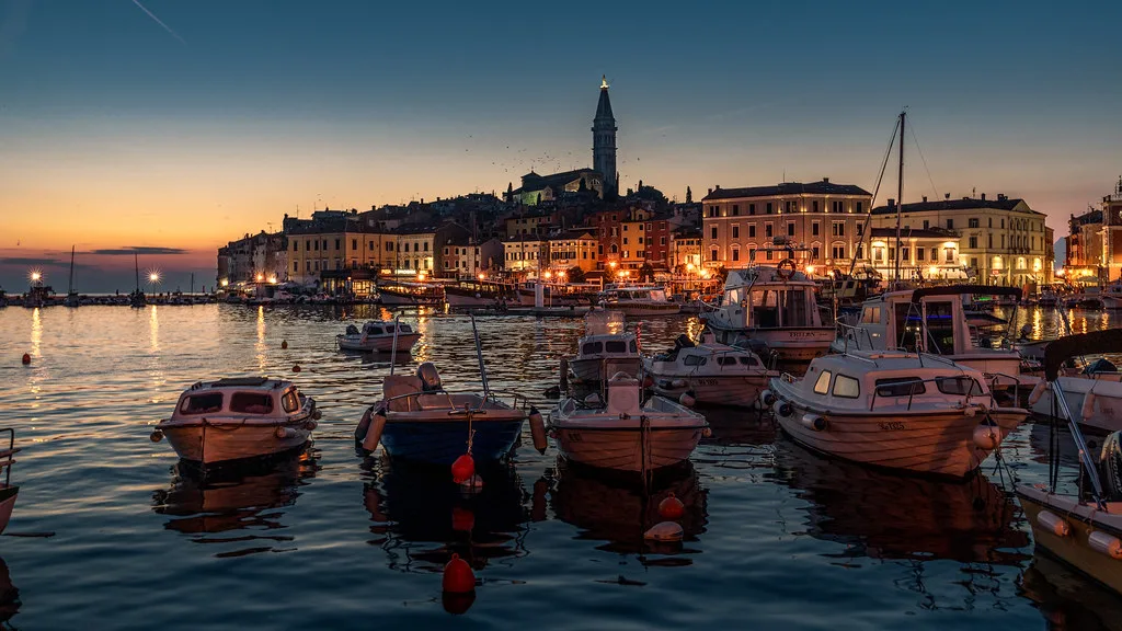 Boats in Rovinj harbour below the lit old town and church tower at dusk, Croatia