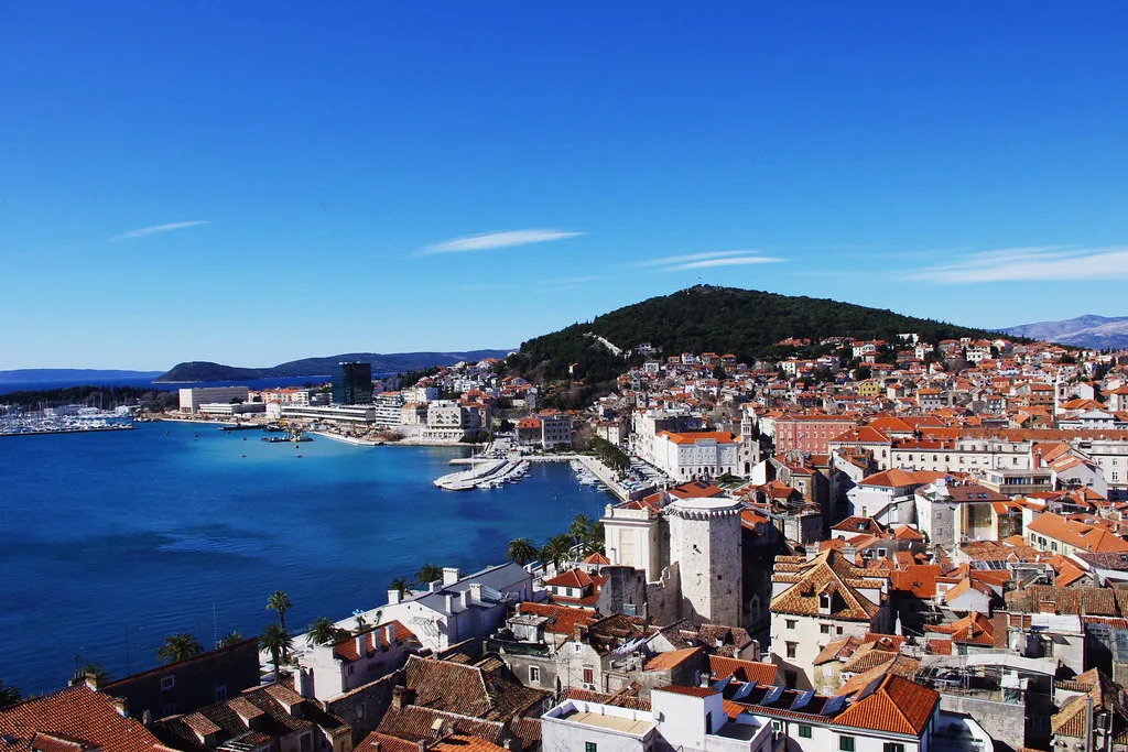 Red-roofed buildings of Split along the harbour, with a wooded hill behind, Croatia