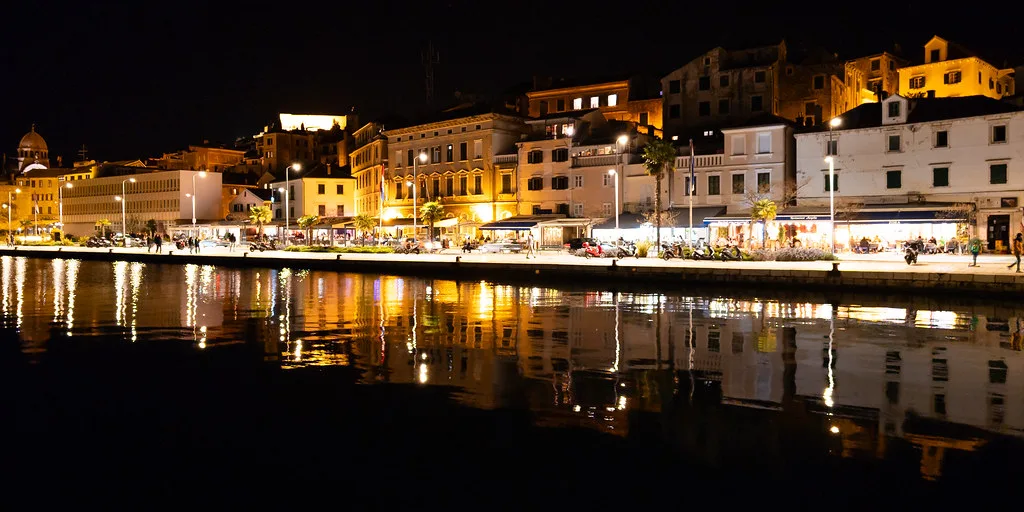 Lit waterfront buildings reflected in the harbour at night in Šibenik