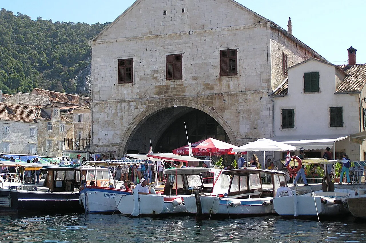 The arched Arsenal building behind small boats moored in the harbour of Hvar Town.
