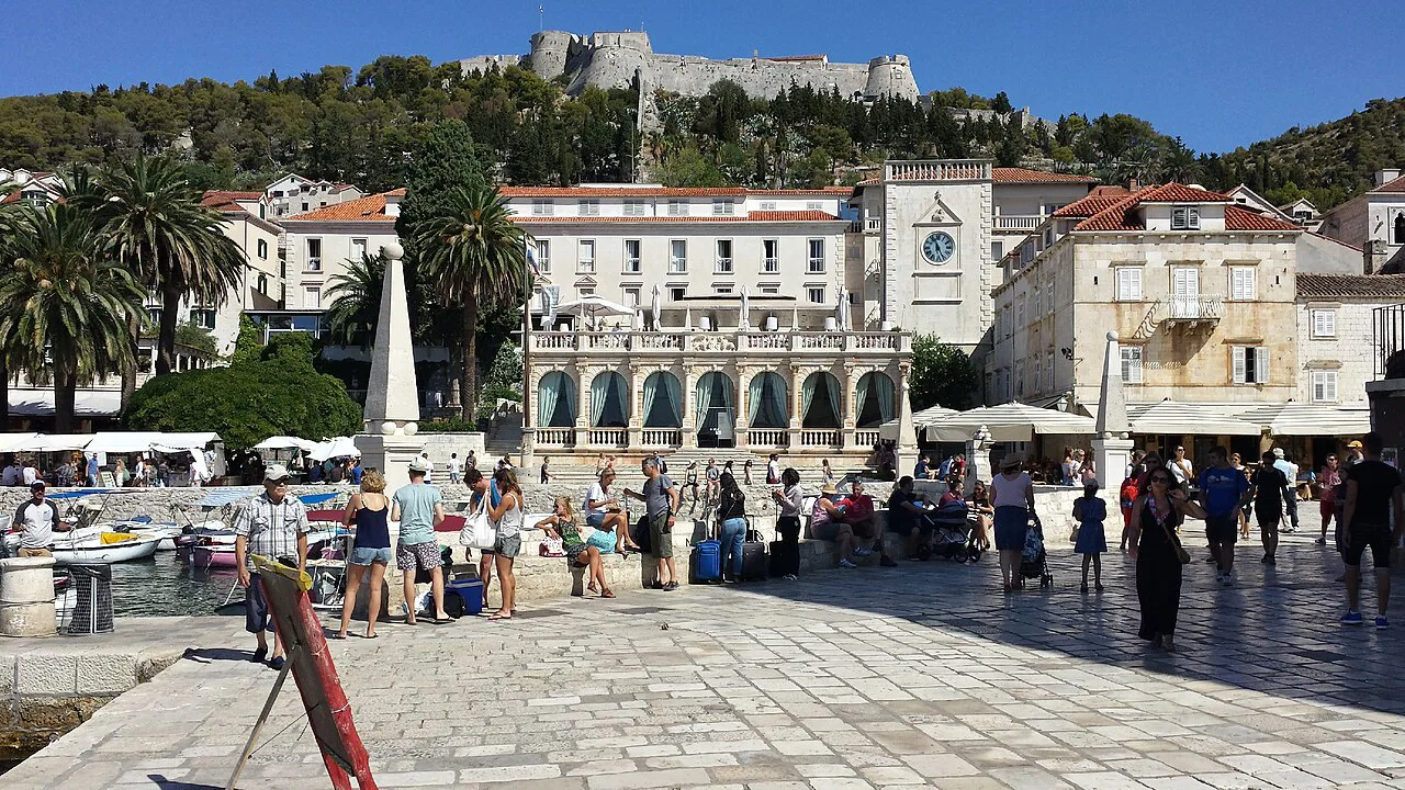 People crossing the main square in Hvar Town with the fortress on the hill above