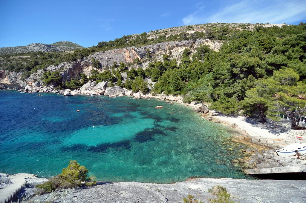 A small cove with clear turquoise water below wooded cliffs on Hvar