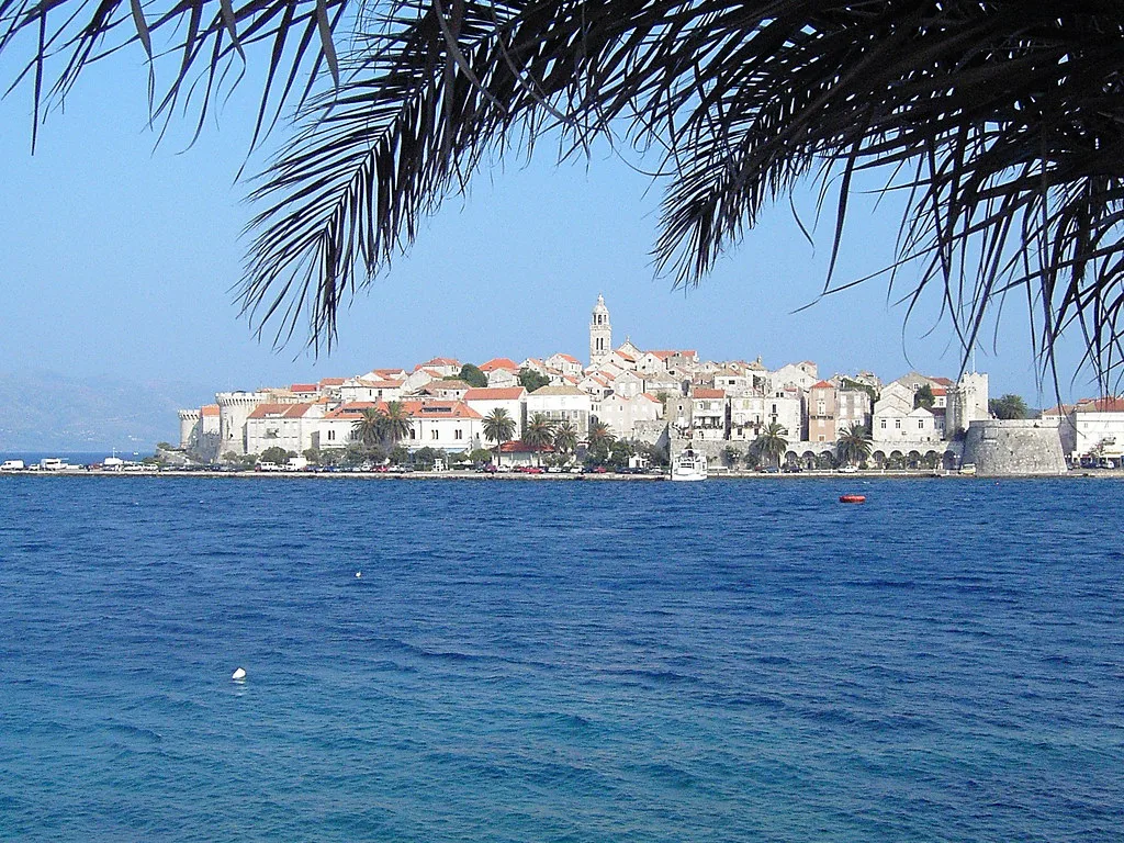 Korčula Old Town on its peninsula seen across the water, framed by palm leaves