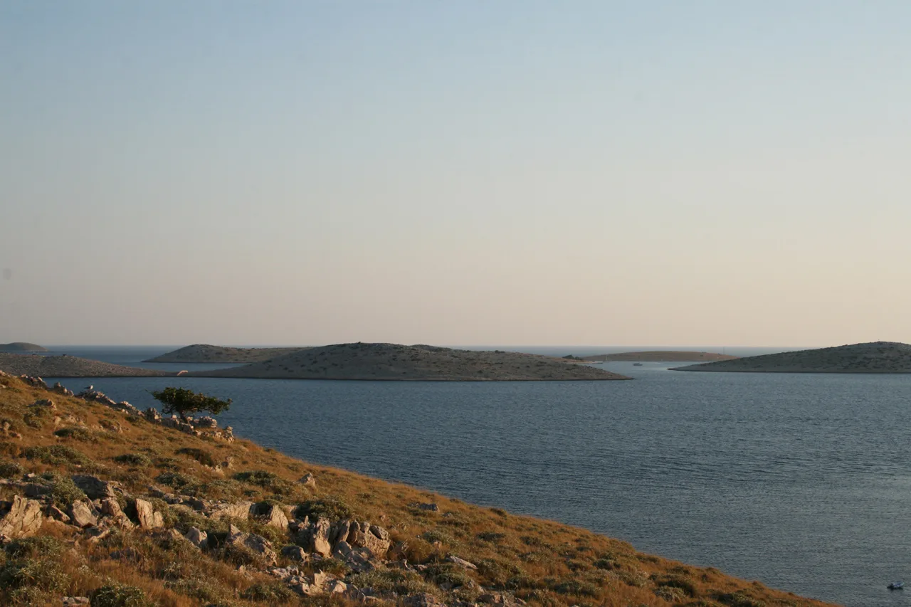Low islands of the Kornati archipelago seen across the sea from a rocky slope, Croatia