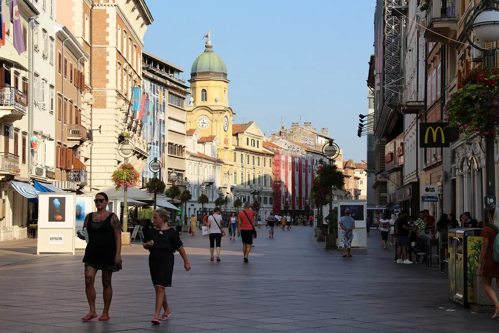 People walking along the Korzo pedestrian street in Rijeka towards the clock tower.