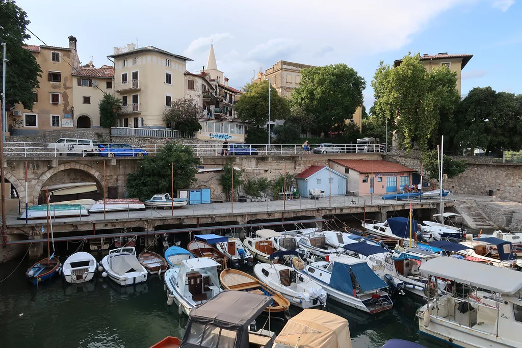Small boats moored in the little harbour of Lovran below old stone houses.
