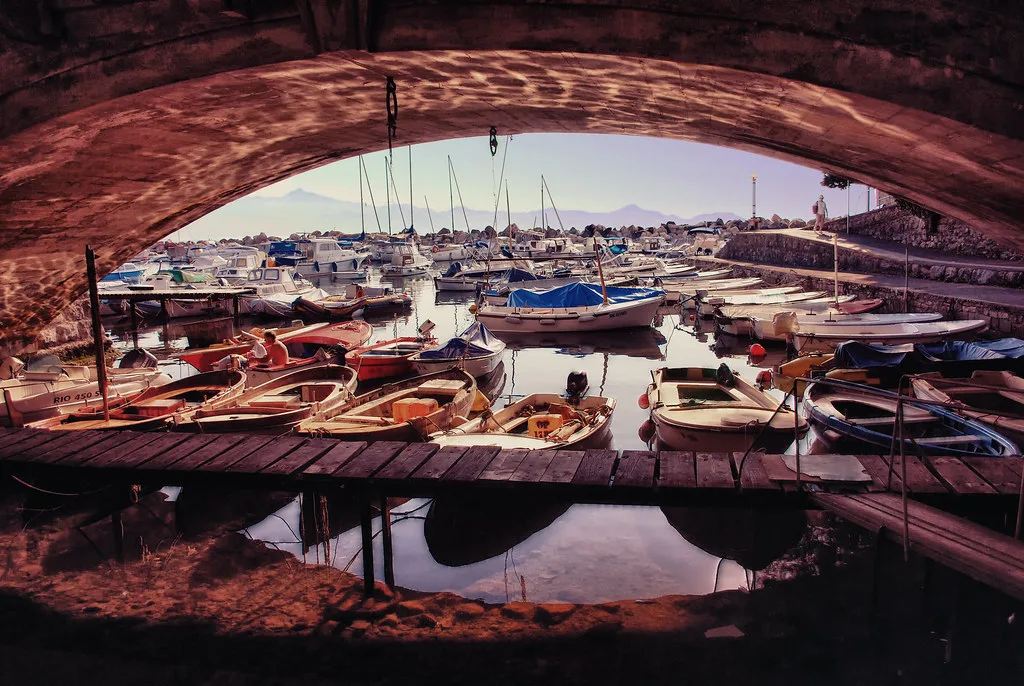 Small boats in the port of Rijeka framed by a stone arch