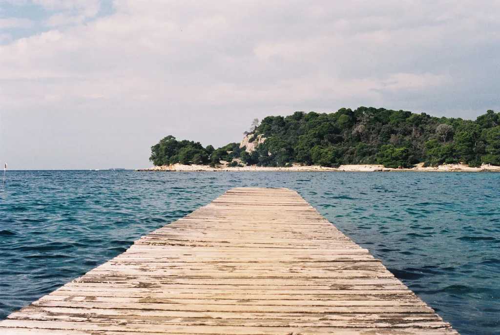 A wooden jetty reaching towards a wooded islet off the coast at Rovinj
