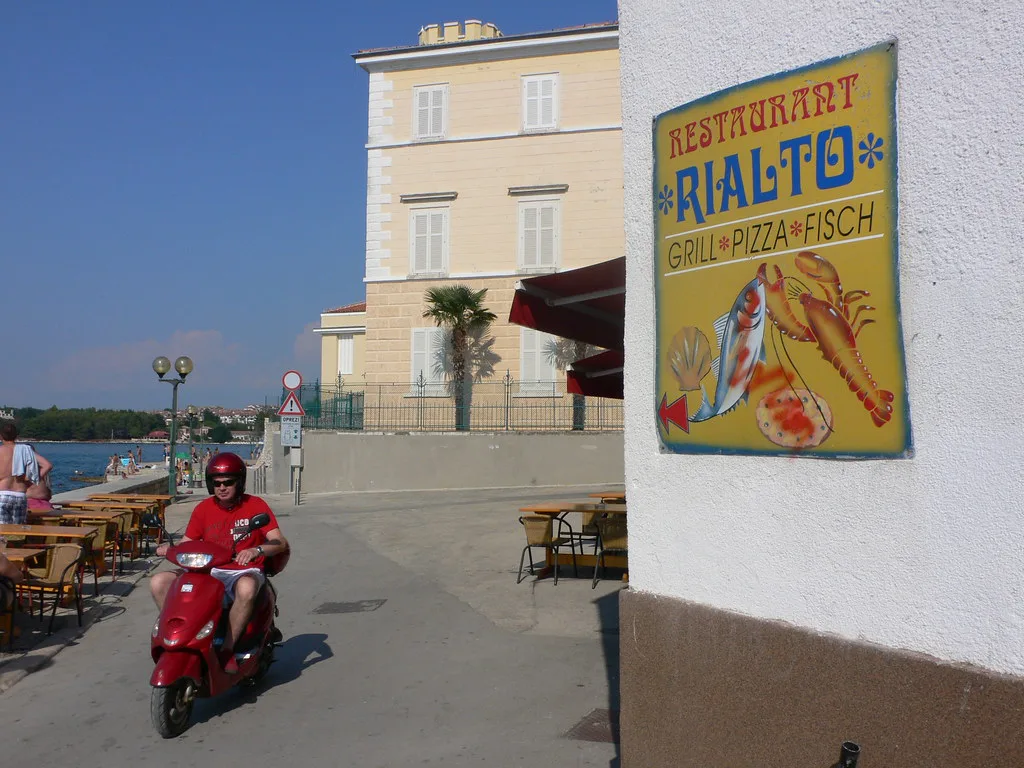 A street with café terraces and a passing scooter in the old town of Poreč