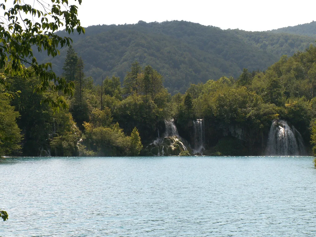 A lake with waterfalls below wooded hills at Plitvice Lakes