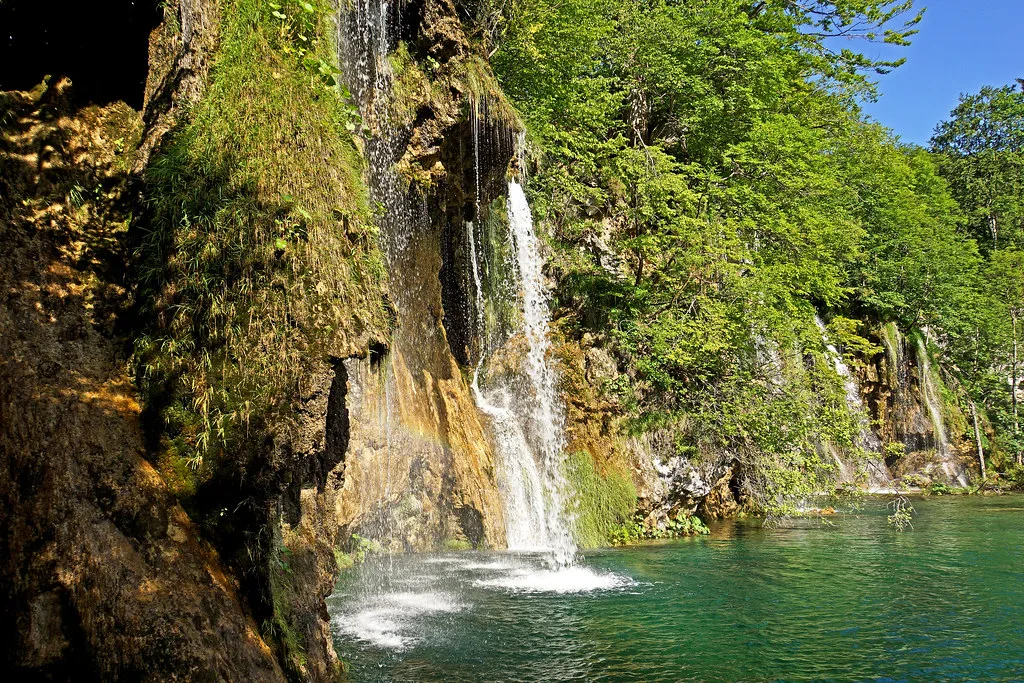 A waterfall dropping into a green pool at Plitvice Lakes