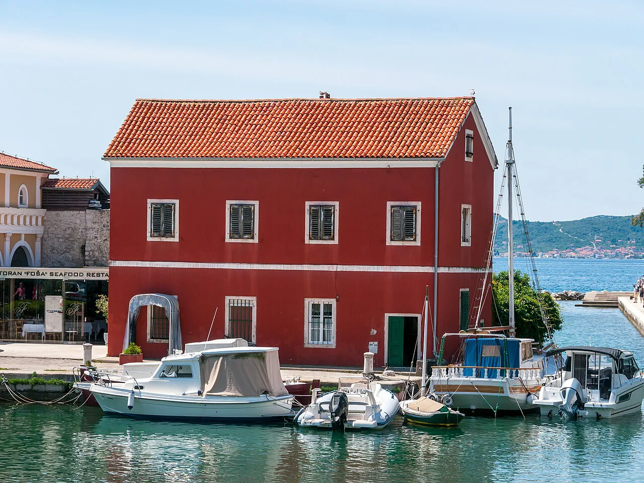 A red building beside small boats moored in the old port of Zadar.