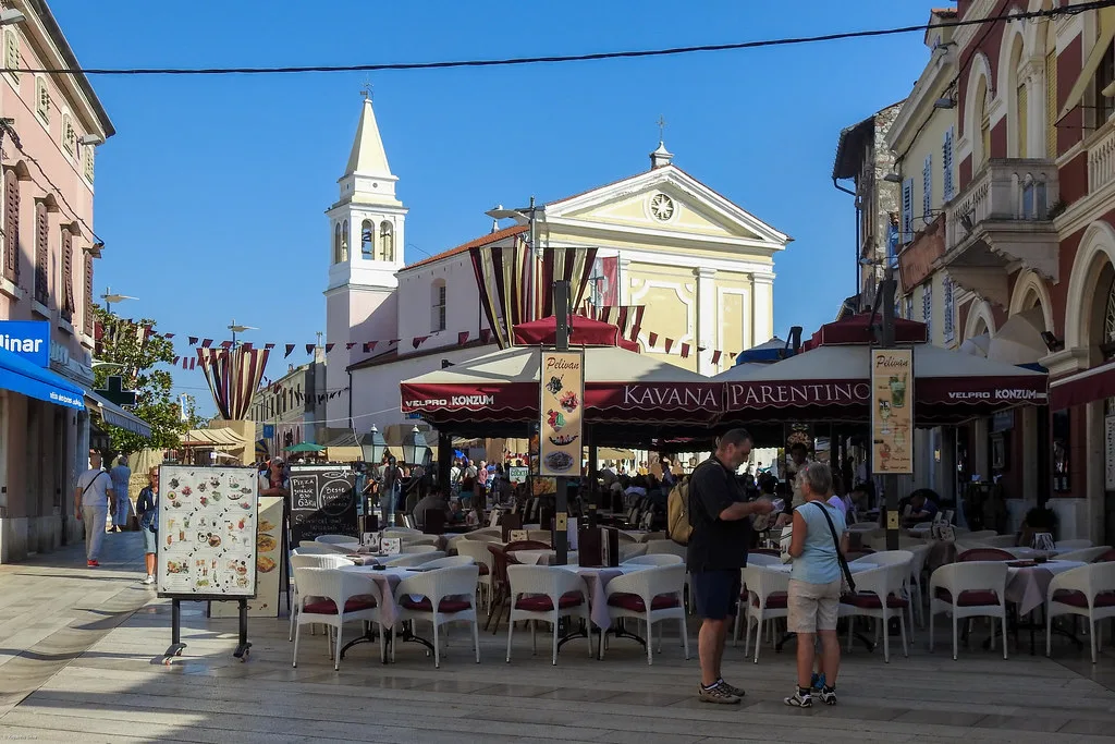Café tables on a square in Poreč's old town below a church and bell tower, Poreč