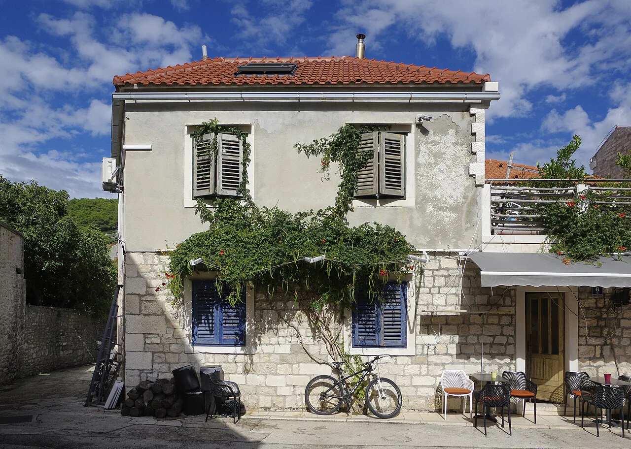 A stone house with green shutters and climbing plants in Pučišća on Brač