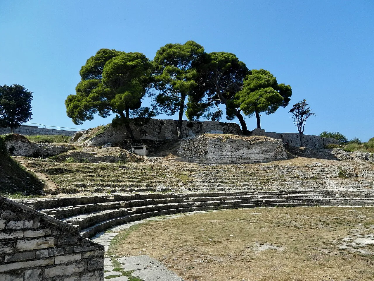 Stone seating of the small Roman theatre in Pula, shaded by pine trees
