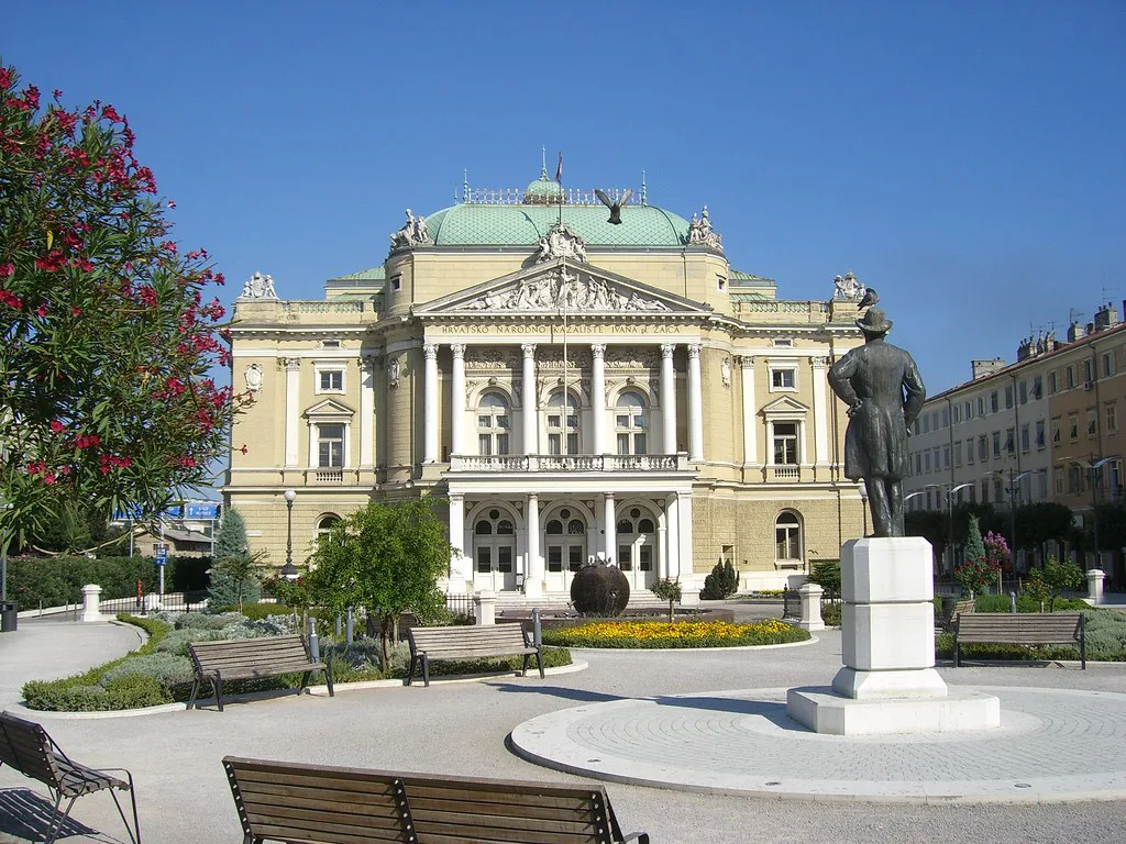 A neoclassical theatre building beside a park in Rijeka