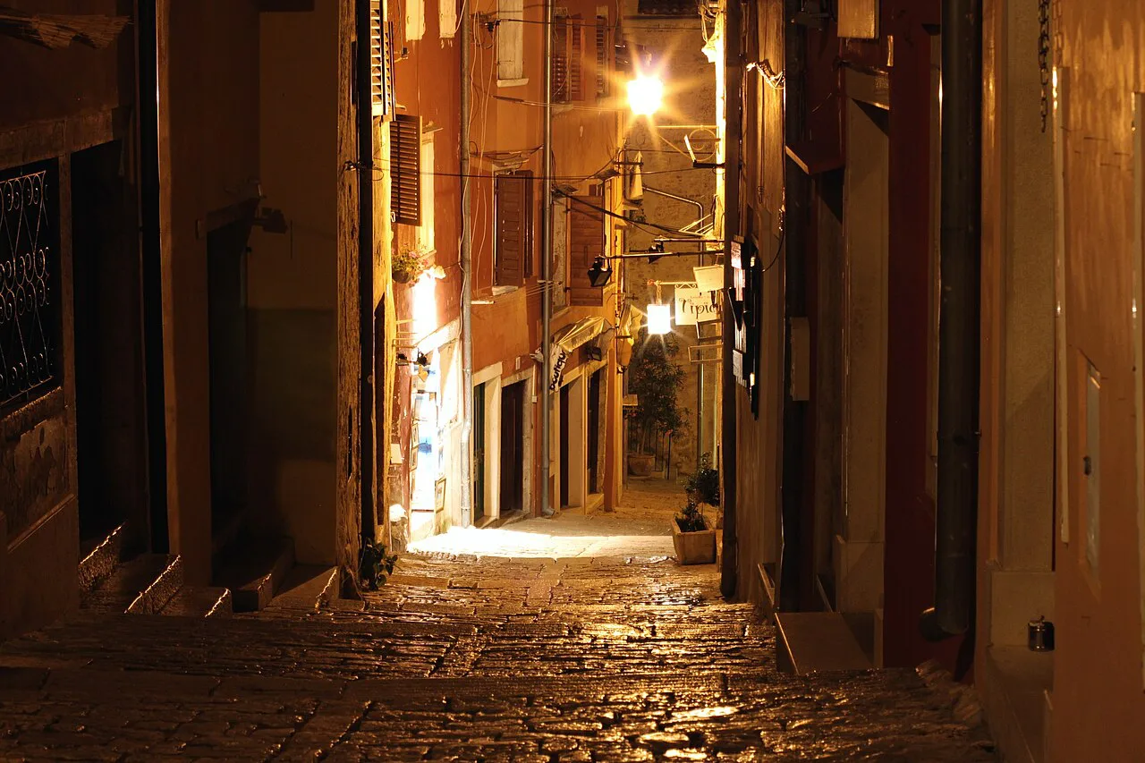 A narrow stone-paved lane lit by street lamps in the old town of Rovinj