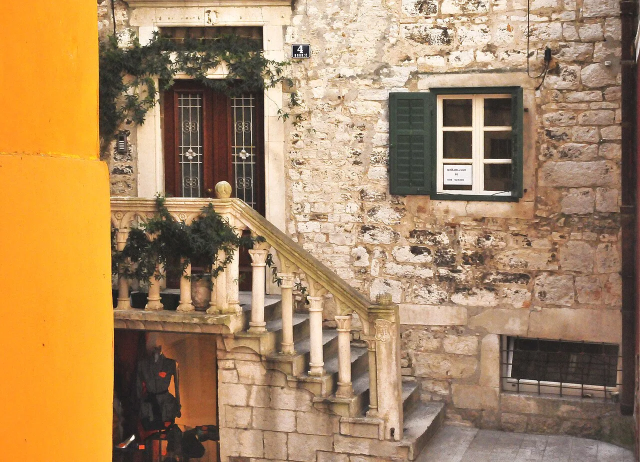 A stone house with an outdoor staircase on a street corner in Šibenik old town
