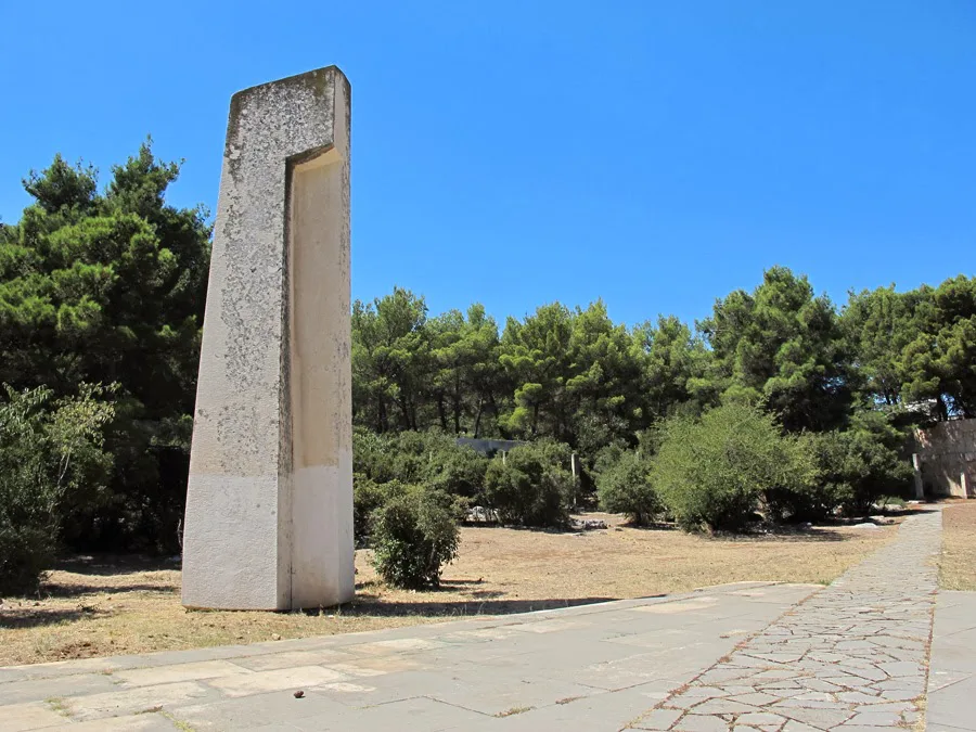 A tall stone monument among pine trees in Šubićevac Memorial Park, Šibenik.