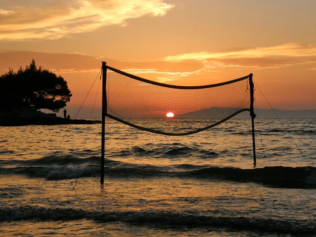 The sun setting over the sea behind a beach volleyball net near Sućuraj on Hvar