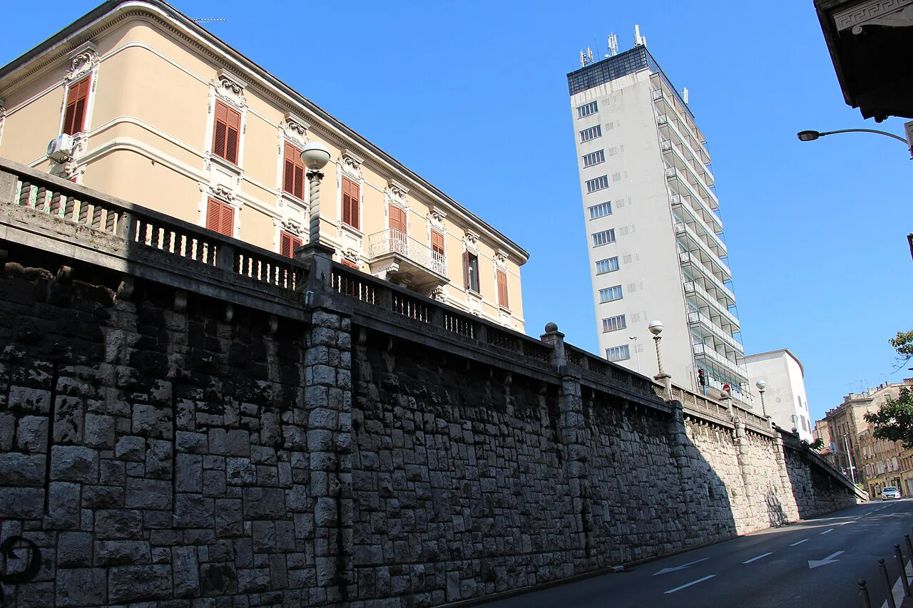 A glass-clad tower block rising behind older buildings on a street in Sušak, Rijeka