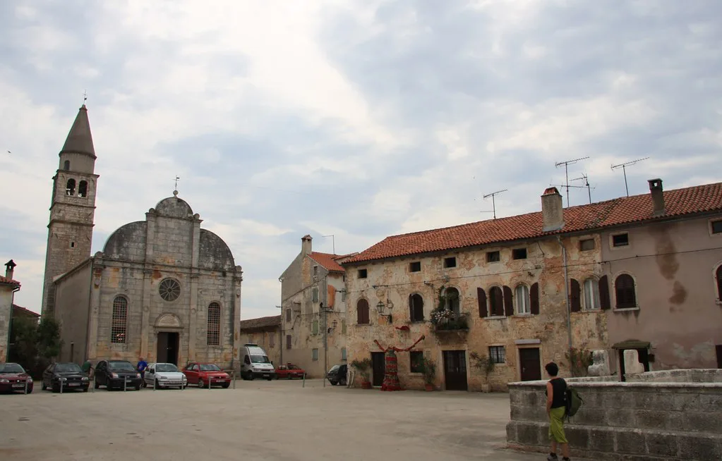 A church with a bell tower beside stone houses on the main square of Svetvinčenat, Istria