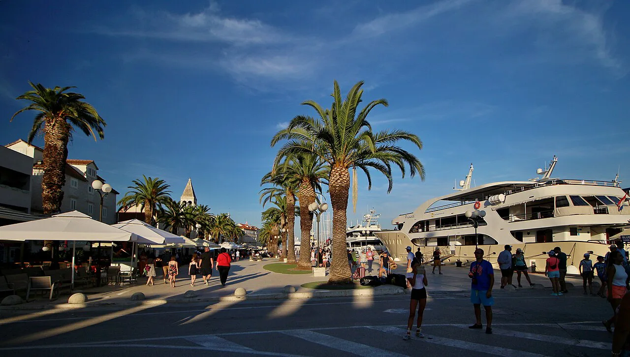 Café umbrellas, palm trees and a moored cruise boat along the Trogir promenade, Dalmatia