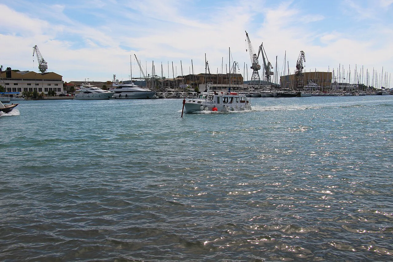 A small boat crossing the harbour channel in Trogir, with marina masts beyond, Dalmatia