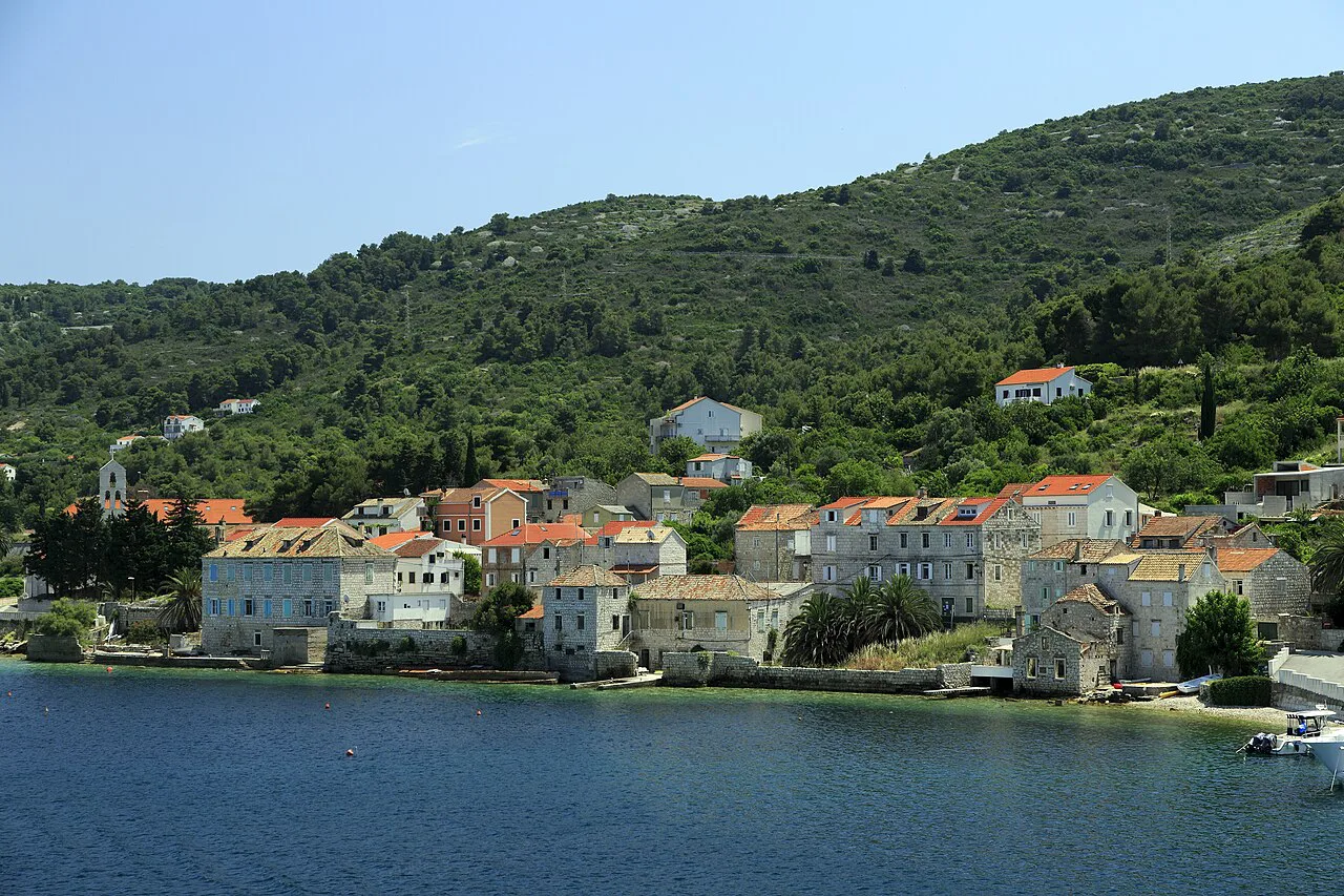 Stone houses along the waterfront of Vis town beneath a wooded hillside
