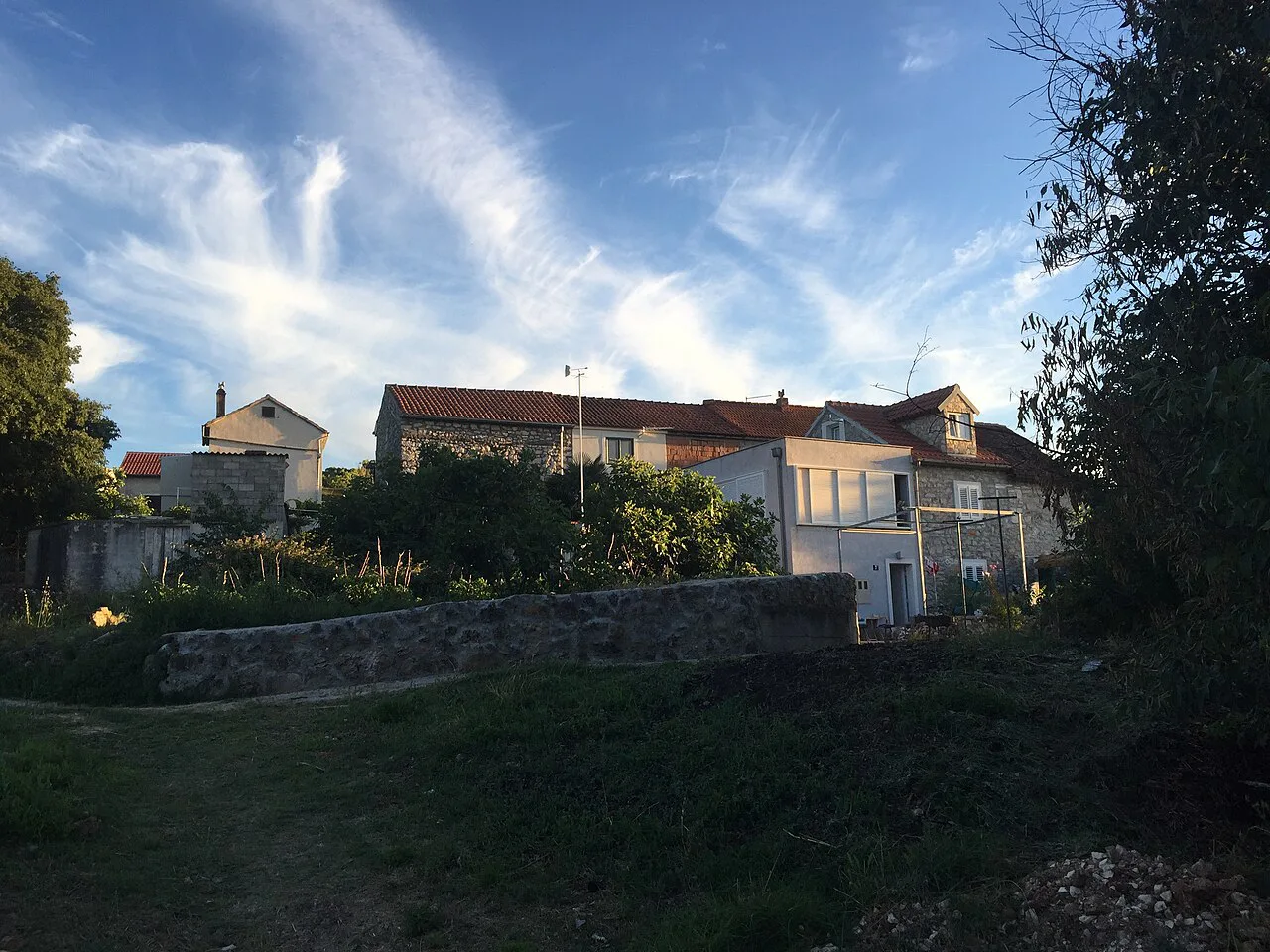 Stone houses behind trees and a garden wall on Zlarin, Šibenik