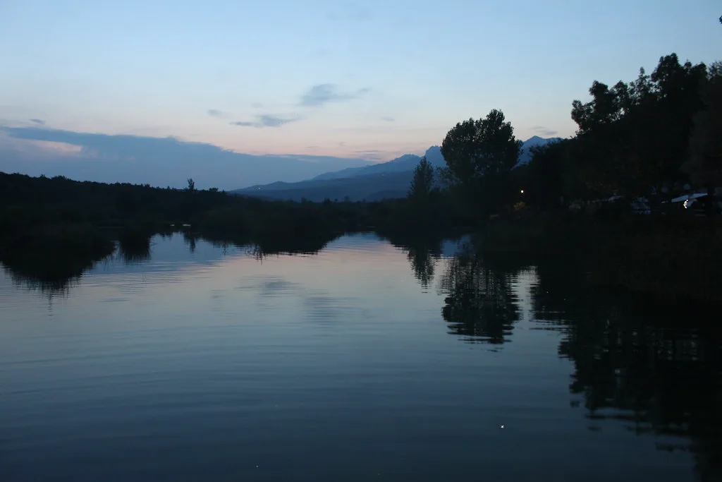 The calm Zrmanja river reflecting wooded banks and hills at dusk, Dalmatia